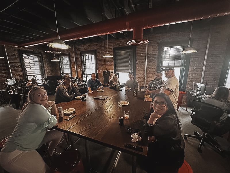 A group of people are sitting around a long table in a room.
