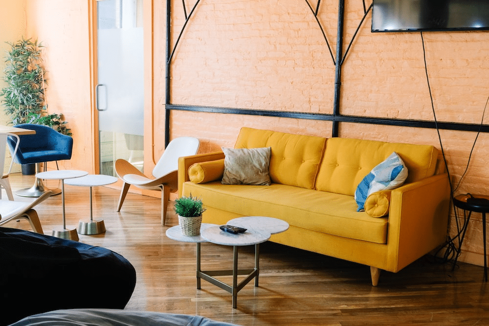 Yellow sofa in a modern lounge with a peach-colored wall, small tables, and seating.