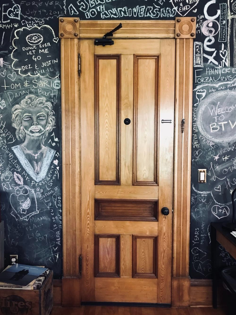 Wooden door with chalkboard walls covered in white drawings and writing.