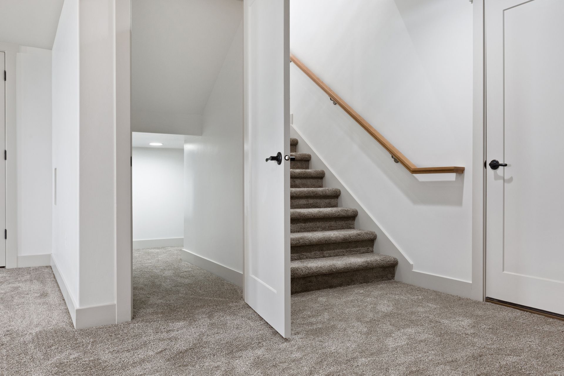 A staircase with carpet steps and a wooden handrail, leading upward from a carpeted hallway.