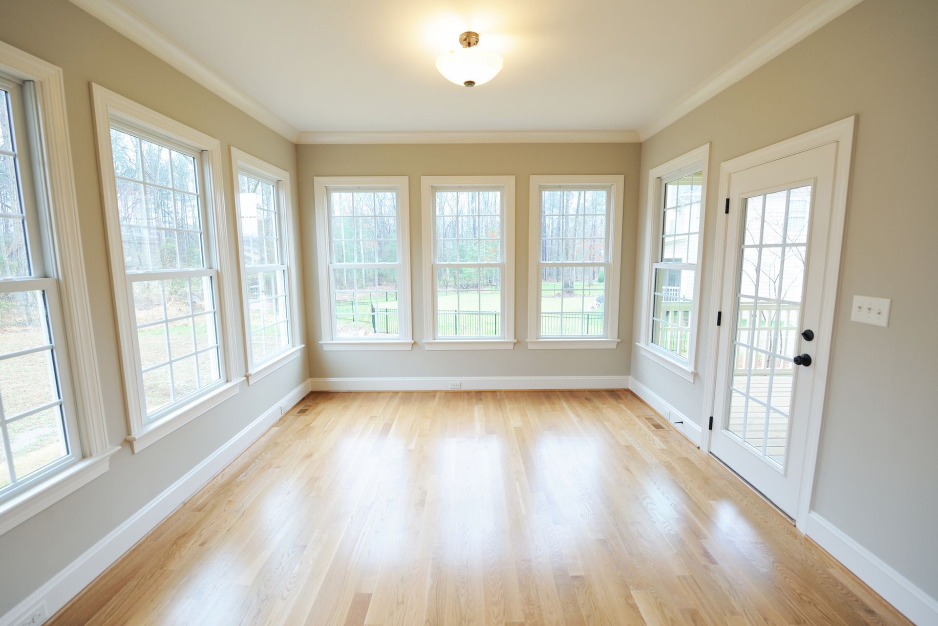 Empty sunroom with hardwood floors, light beige walls, and numerous windows.