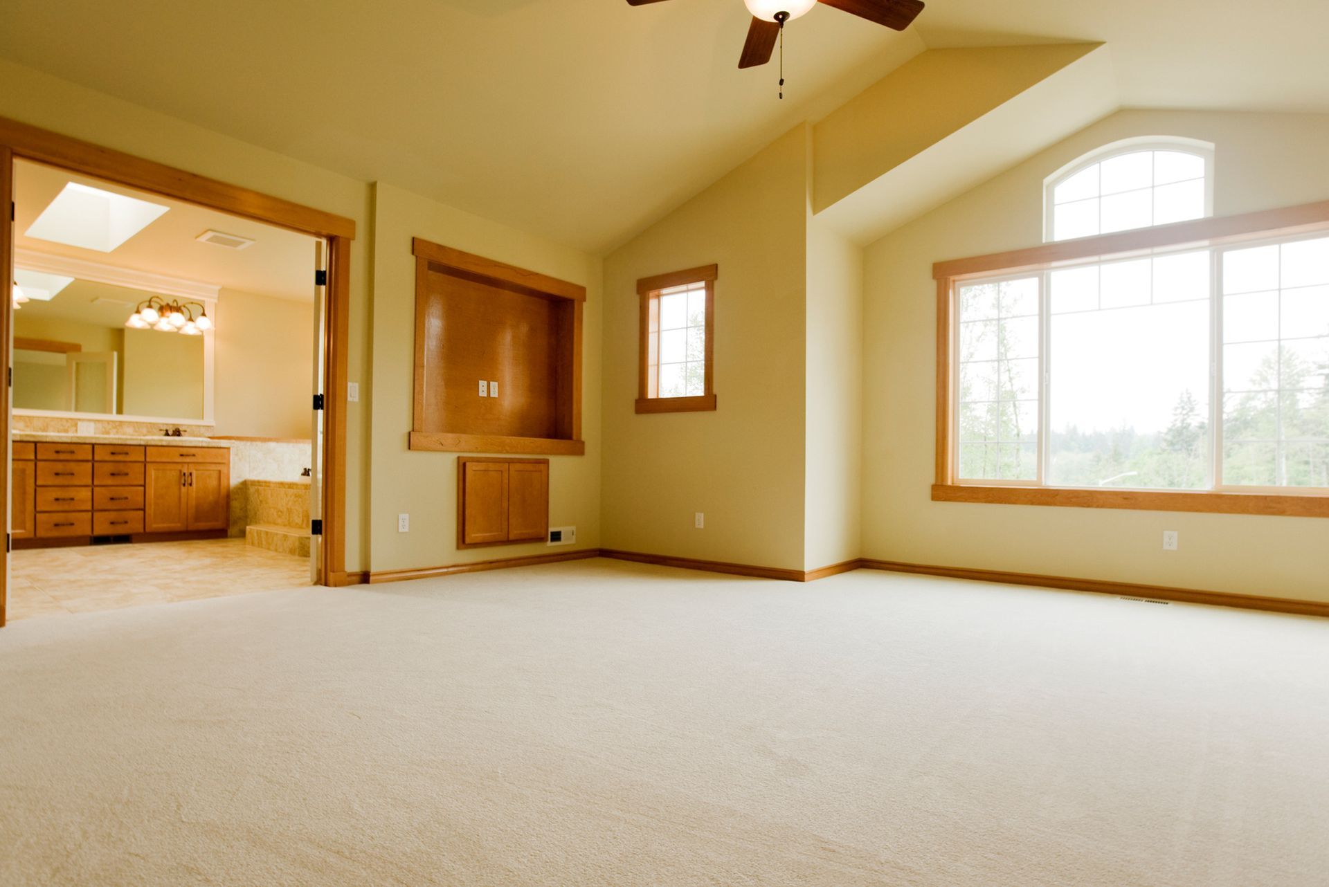 Empty, neutral-toned bedroom with large windows and a door leading to a bathroom with wooden cabinetry. Empty, neutral-toned bedroom with large windows and a door leading to a bathroom with wooden cabinetry.