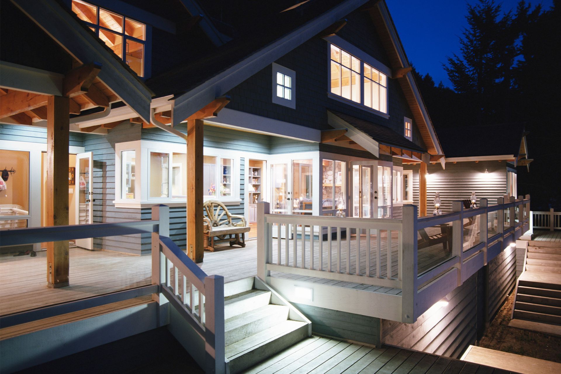 Night view of a house with a deck, lit windows, and stairs. Night view of a house with a deck, lit windows, and stairs.