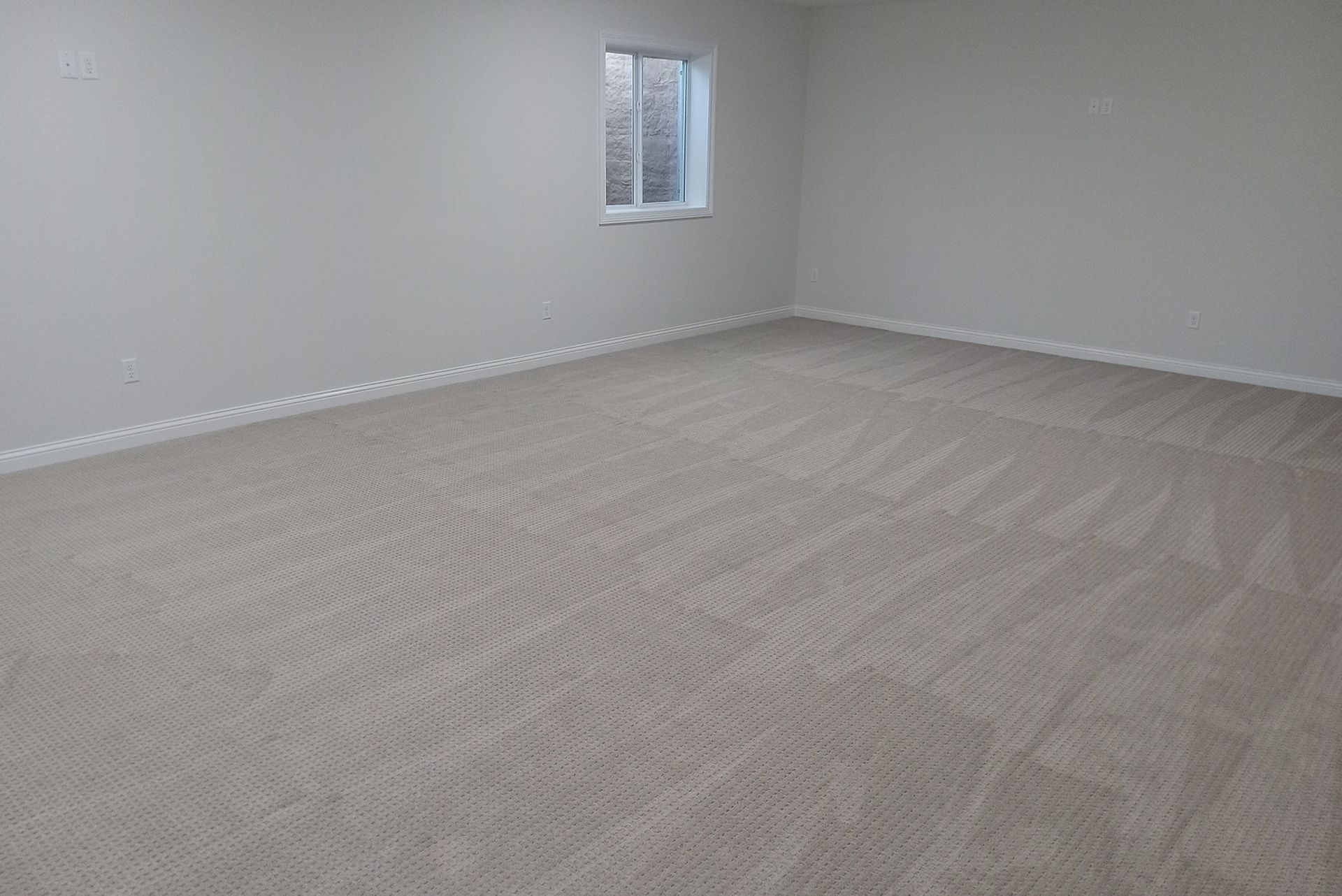 Empty room with beige carpet and off-white walls. Small window on the far wall. Empty room with beige carpet and off-white walls. Small window on the far wall.