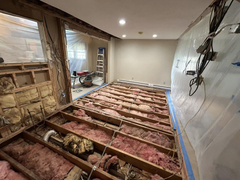 Room under renovation with exposed floor joists, pink insulation, and unfinished walls