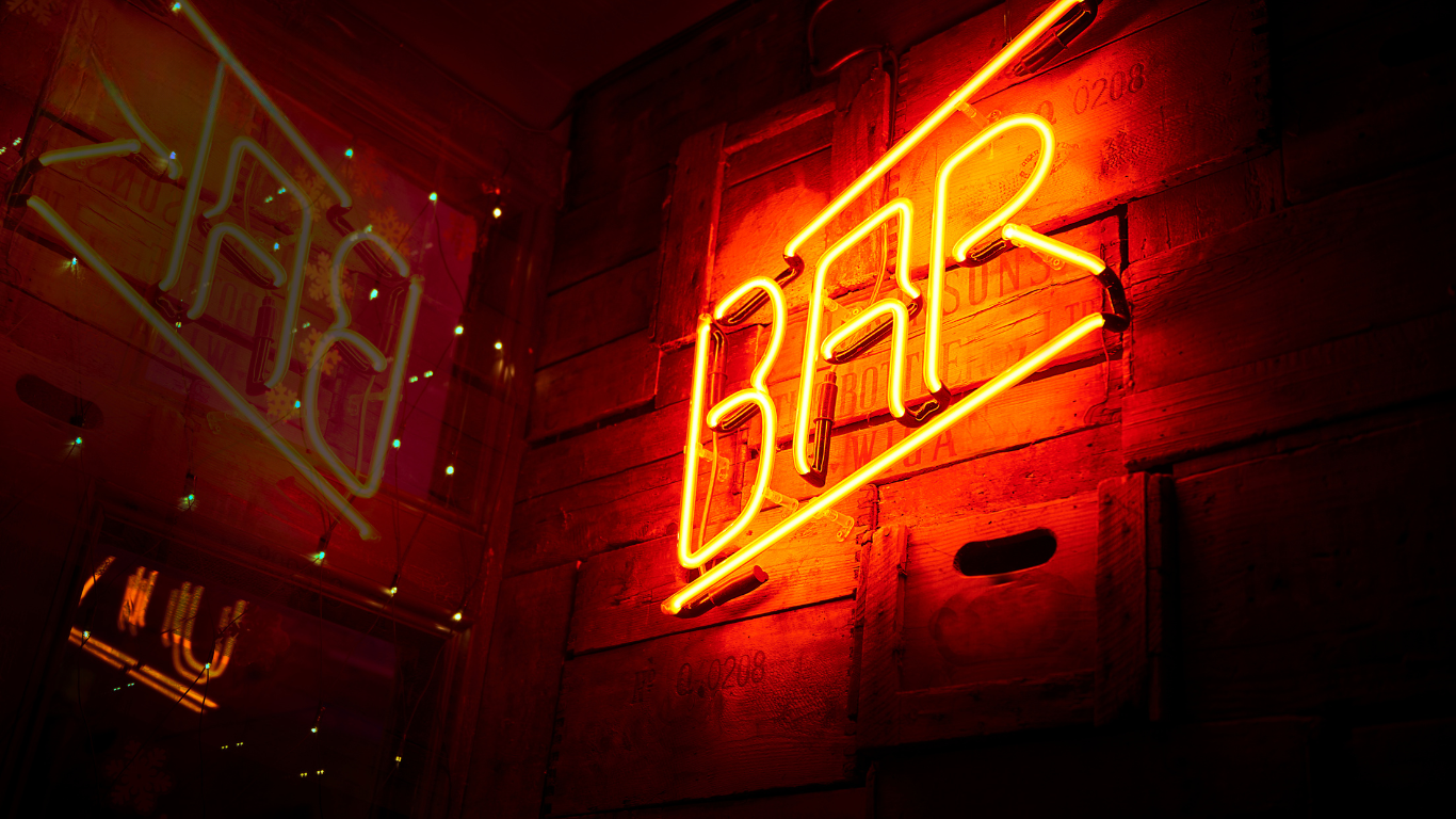 A neon sign that says bar is lit up on a brick wall.