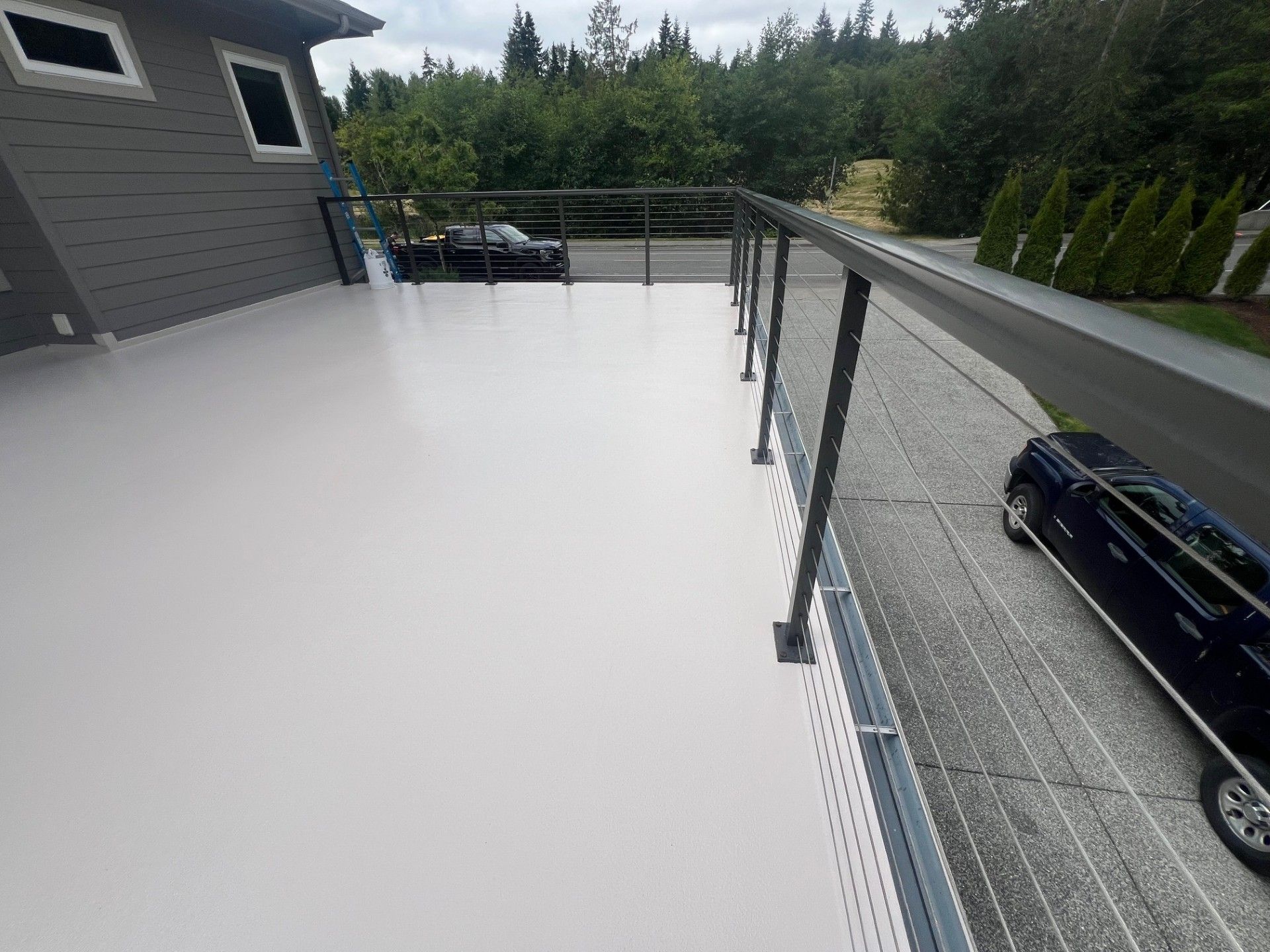 Light gray deck with black railing, overlooks a driveway and trees.