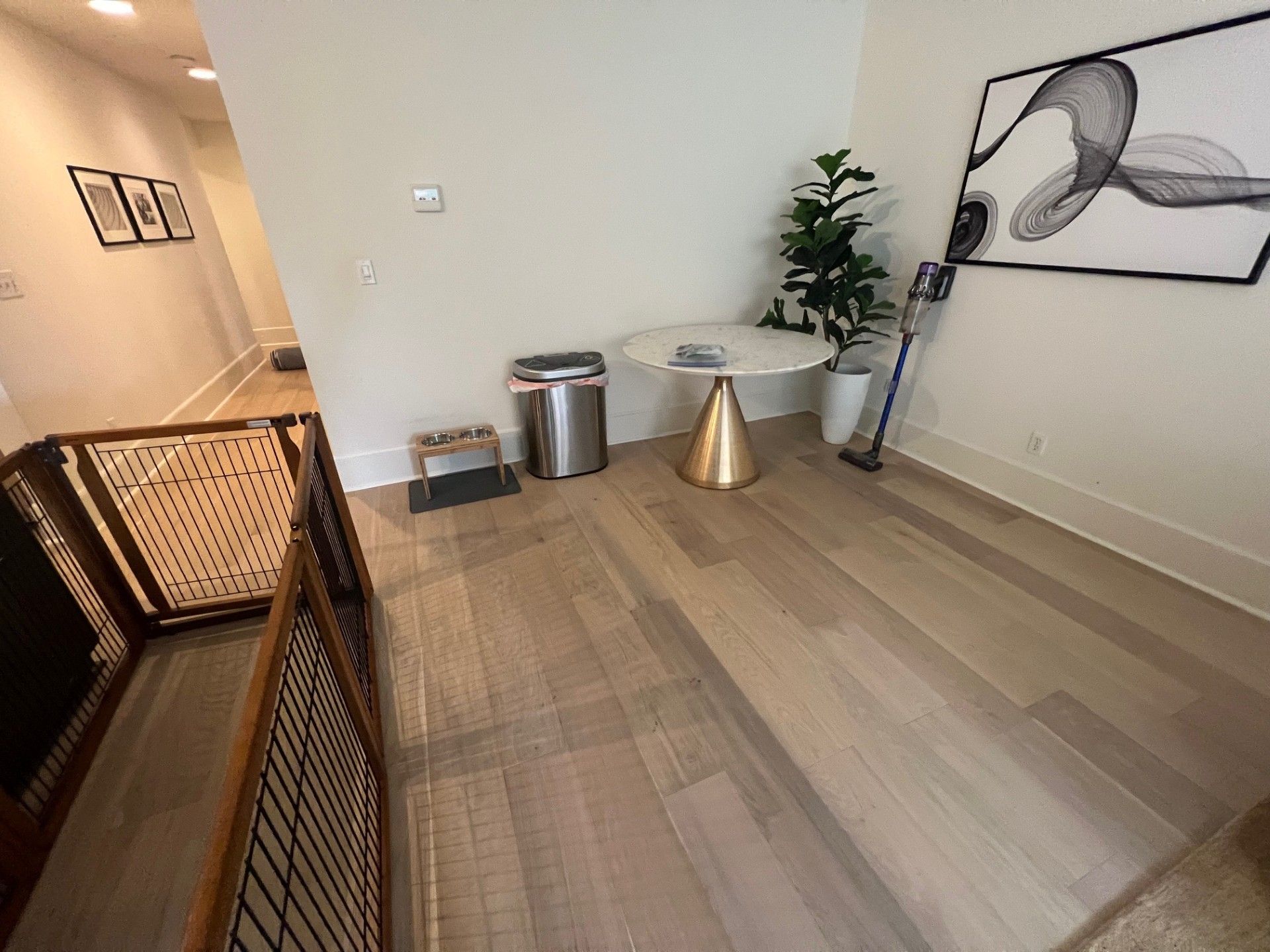 A light-filled room with hardwood floors, a small table, a dog gate, and a houseplant.