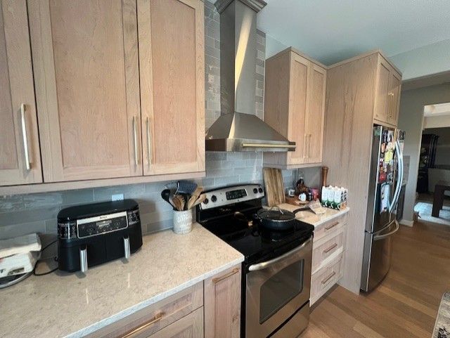 Light wood kitchen with stainless steel appliances. Air fryer and cutting board on countertops.