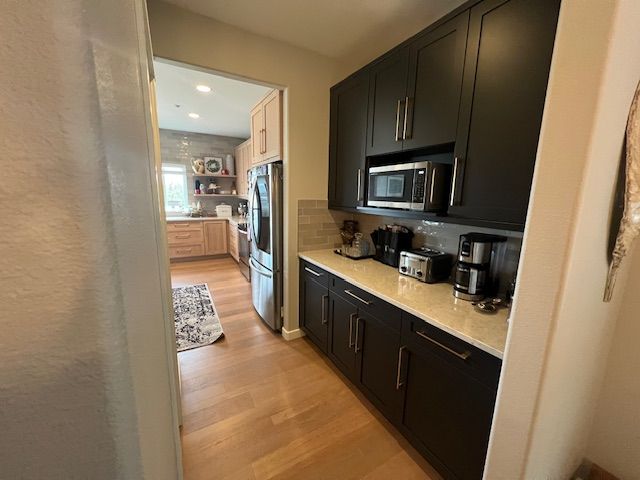 Black cabinets with countertop appliances in a kitchen, doorway to a light-colored kitchen beyond.