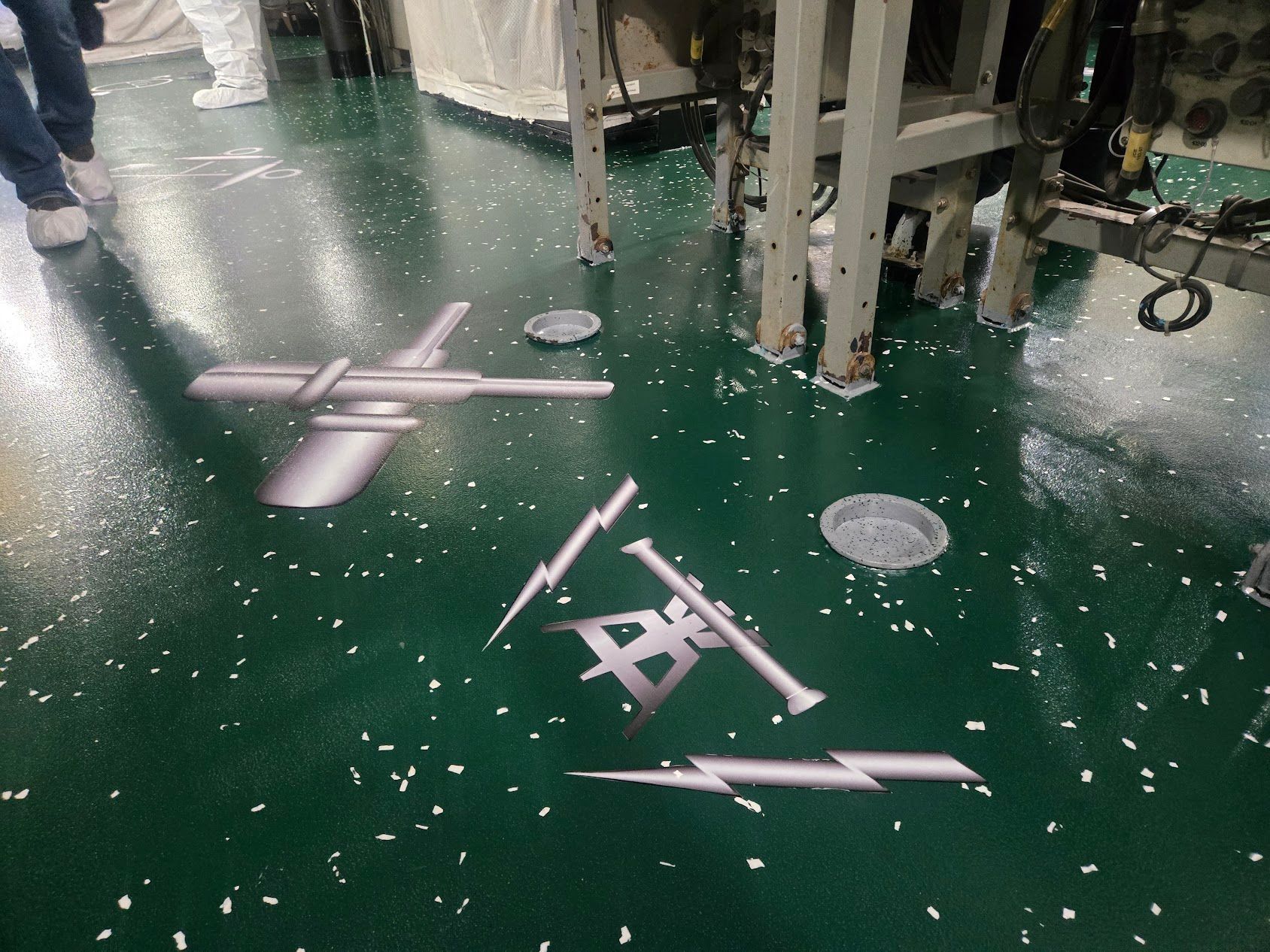 Green industrial floor with graphic decals of a plane, lightning bolts, and parts. White debris scattered.