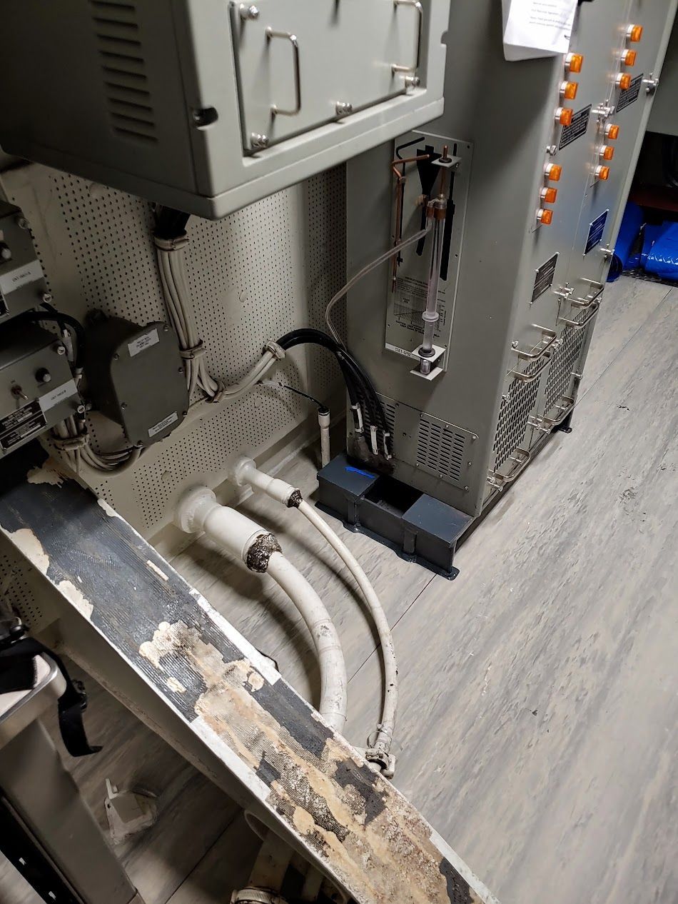 Close-up view of industrial equipment, with cables and wiring, set against a speckled wall and floor.