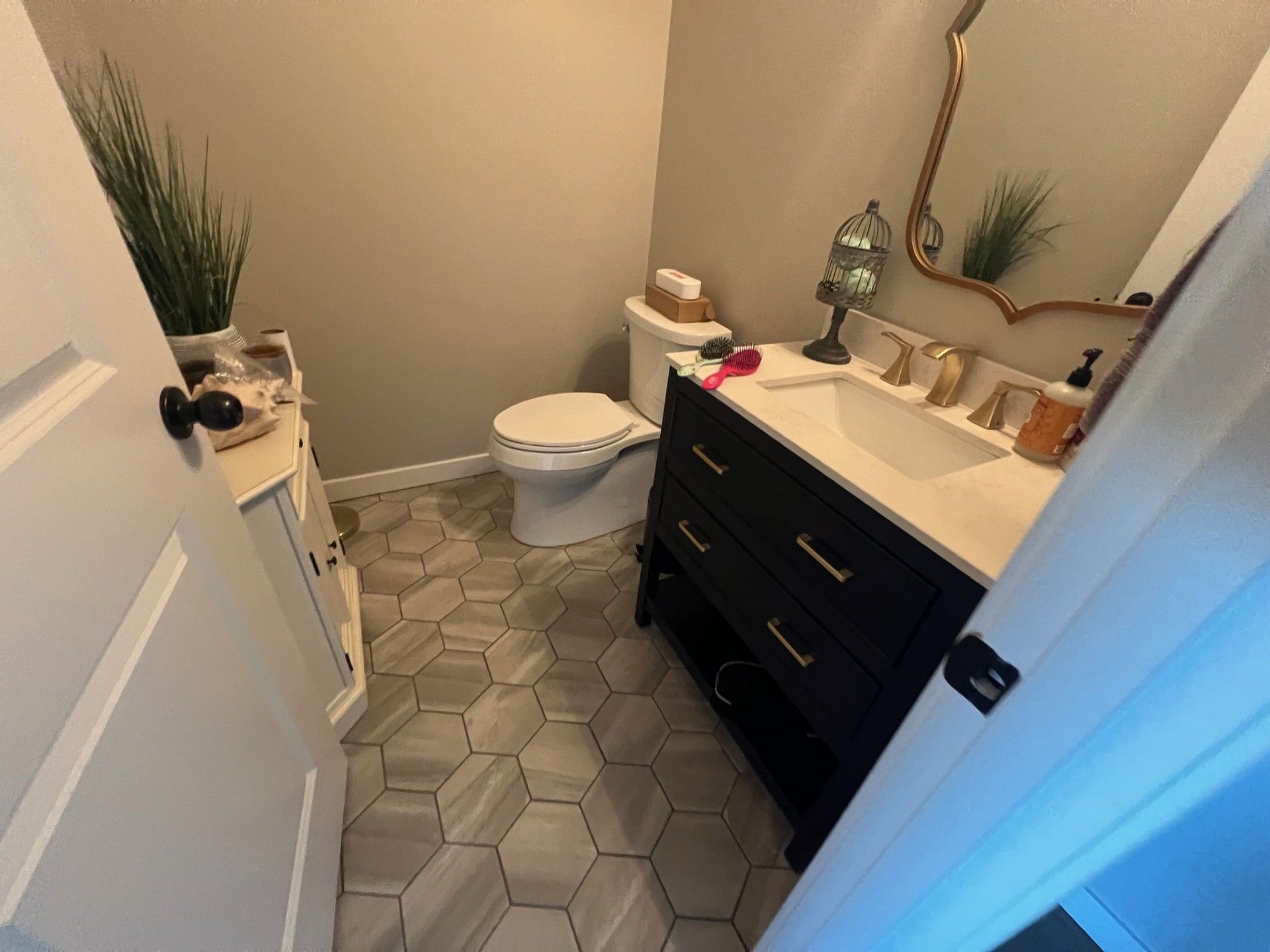 Bathroom with a black vanity, gold mirror, white toilet, and patterned floor.