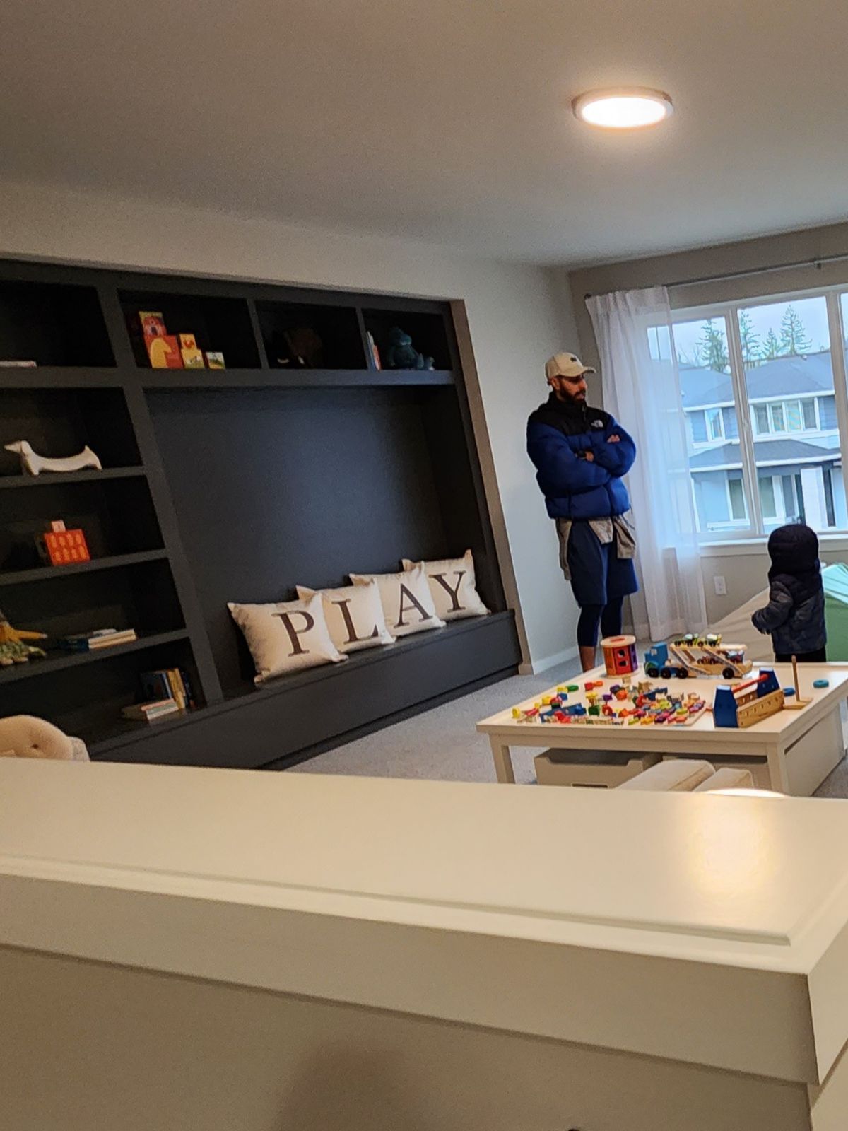 Man watches child playing with Legos near a built-in bookshelf, with 