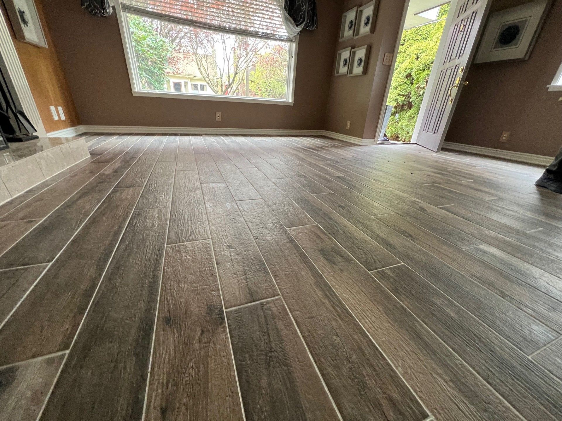 Wooden-look tile floor in a room with a window and open doorway. Dark brown with grout lines.