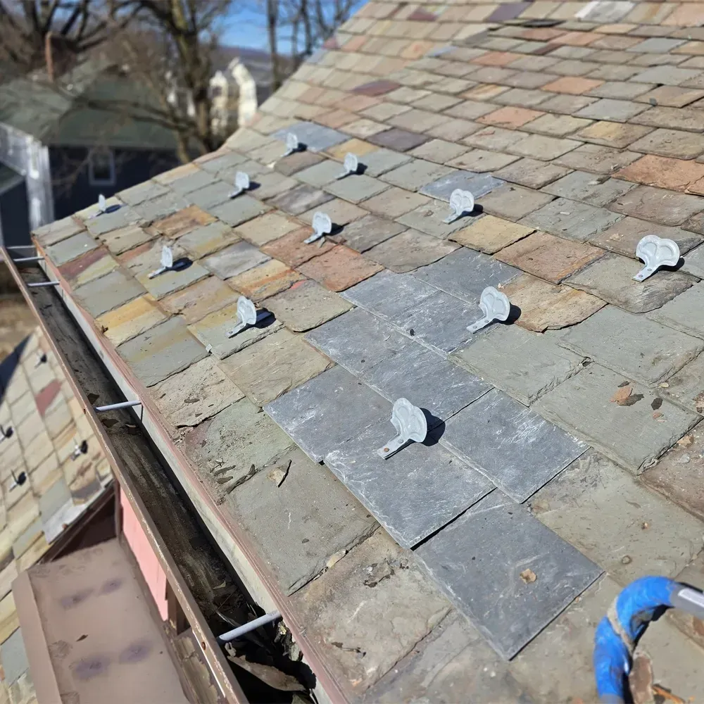A slate roof under repair with metal snow guards and replacement tiles installed.