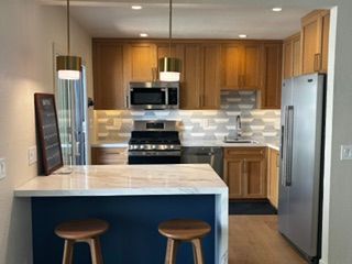 White kitchen with island, black granite countertop, stainless steel appliances, and wooden bar stools.