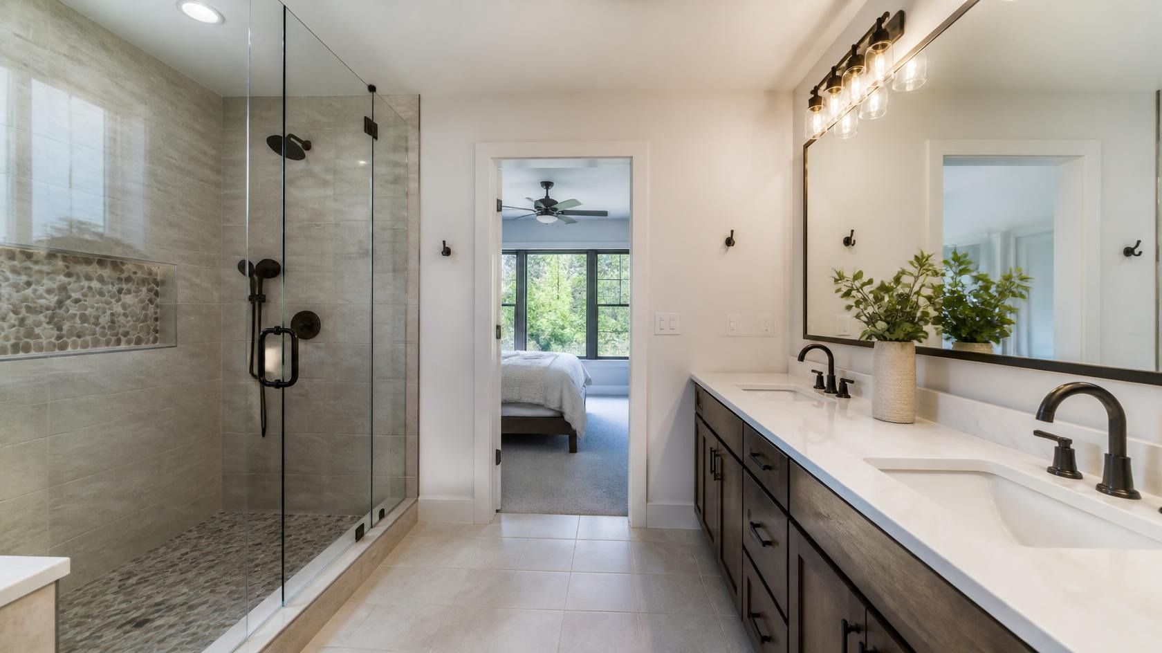 Elegant white bathroom with freestanding tub, glass shower, double sinks, and window.
