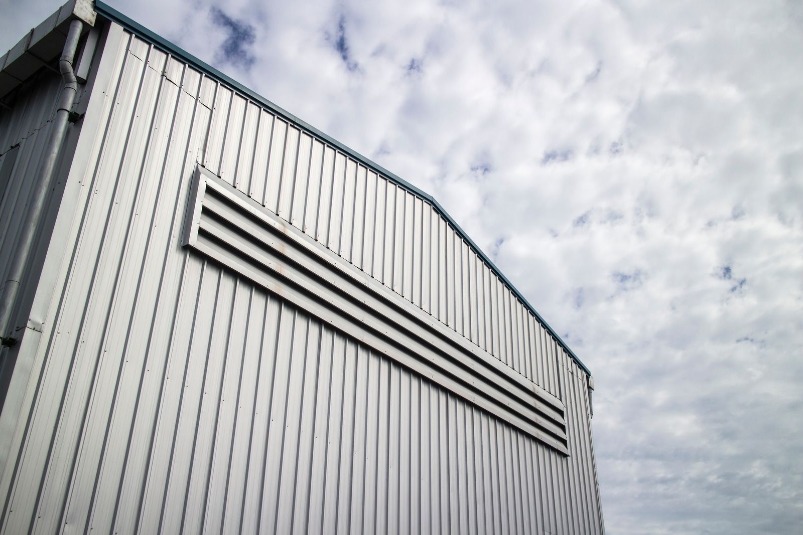 Silver metal building exterior with air vent, against a cloudy sky.
