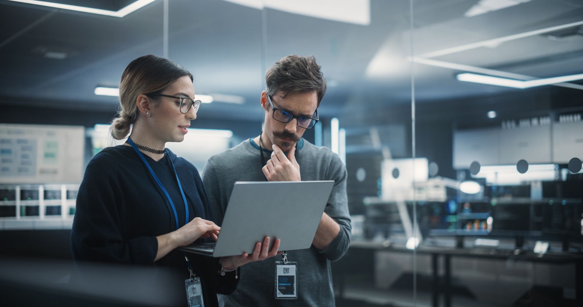 Woman and man looking at a laptop, possibly in an office setting. Both wearing glasses, focused.
