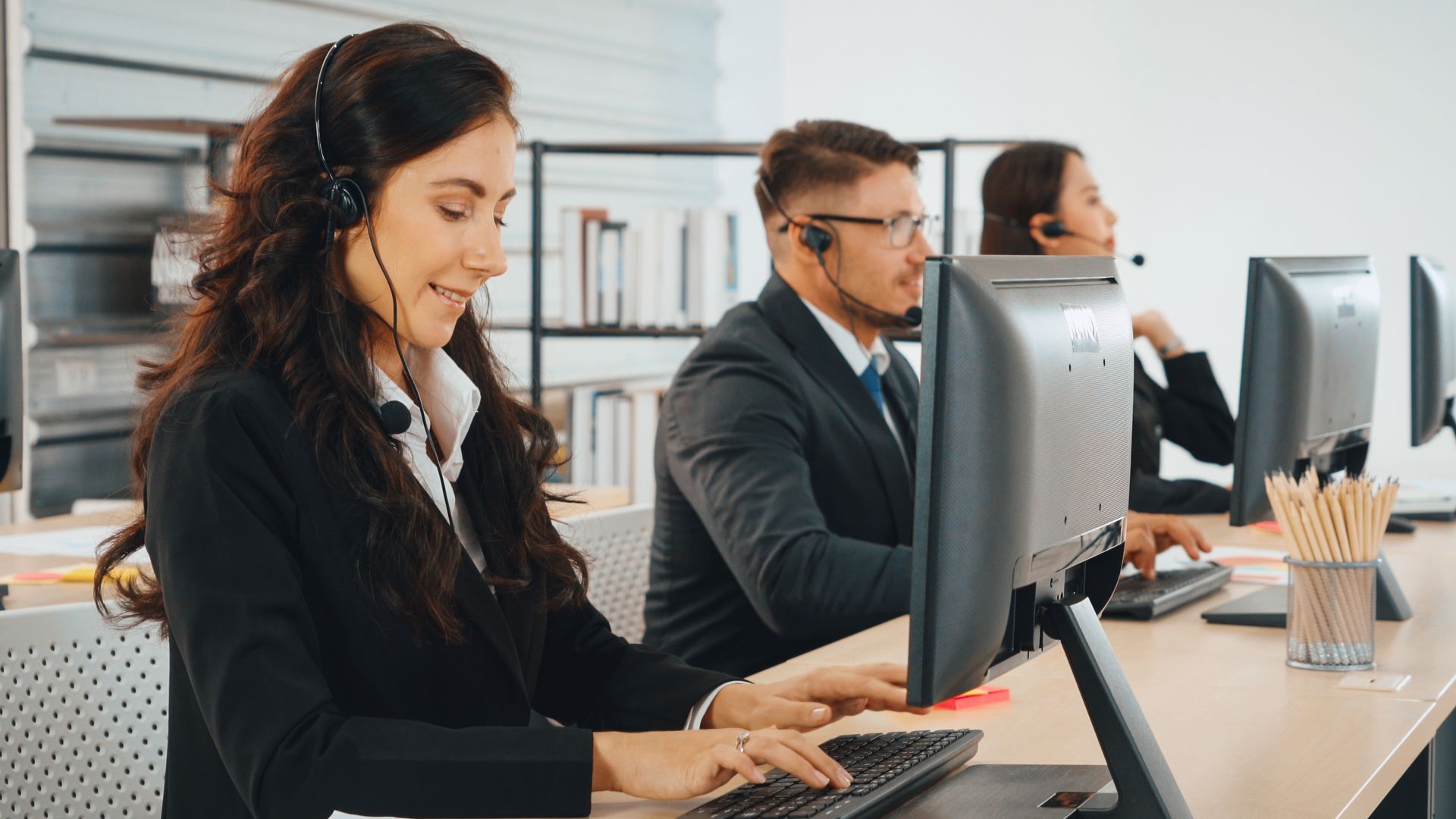 People in headsets working at computers in an office setting.