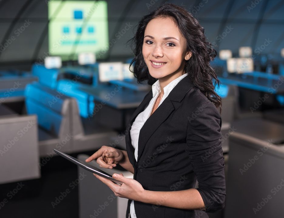 Woman in blazer smiles, using a tablet in a technology-filled room.