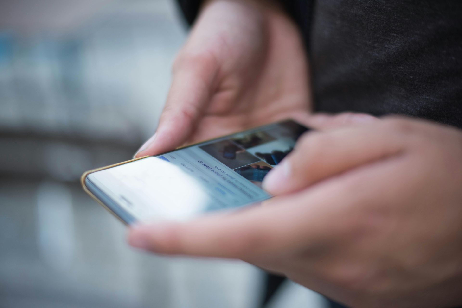 Handen die een smartphone vasthouden en het scherm aanraken, in een buitenomgeving.