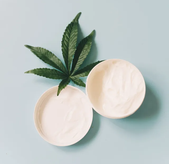 A green cannabis leaf next to open jars of white topical cream - Flo Dispensary 