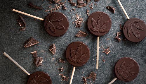 Round chocolate lollipops stamped with cannabis leaves amid chocolate shards --Flo Dispensary