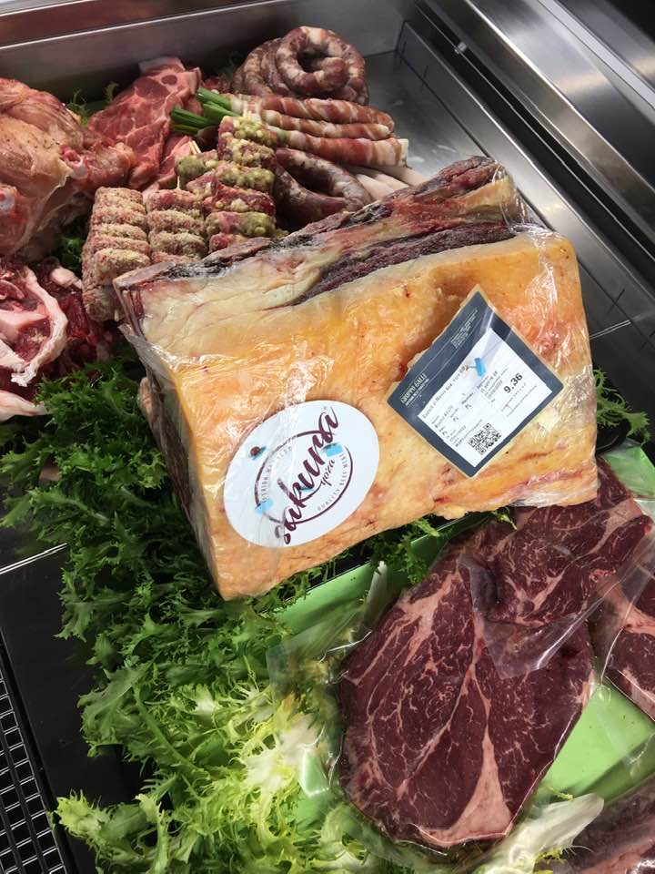 Esposizione di vari tagli di carne cruda, tra cui una grande bistecca confezionata, in un banco gastronomia.
