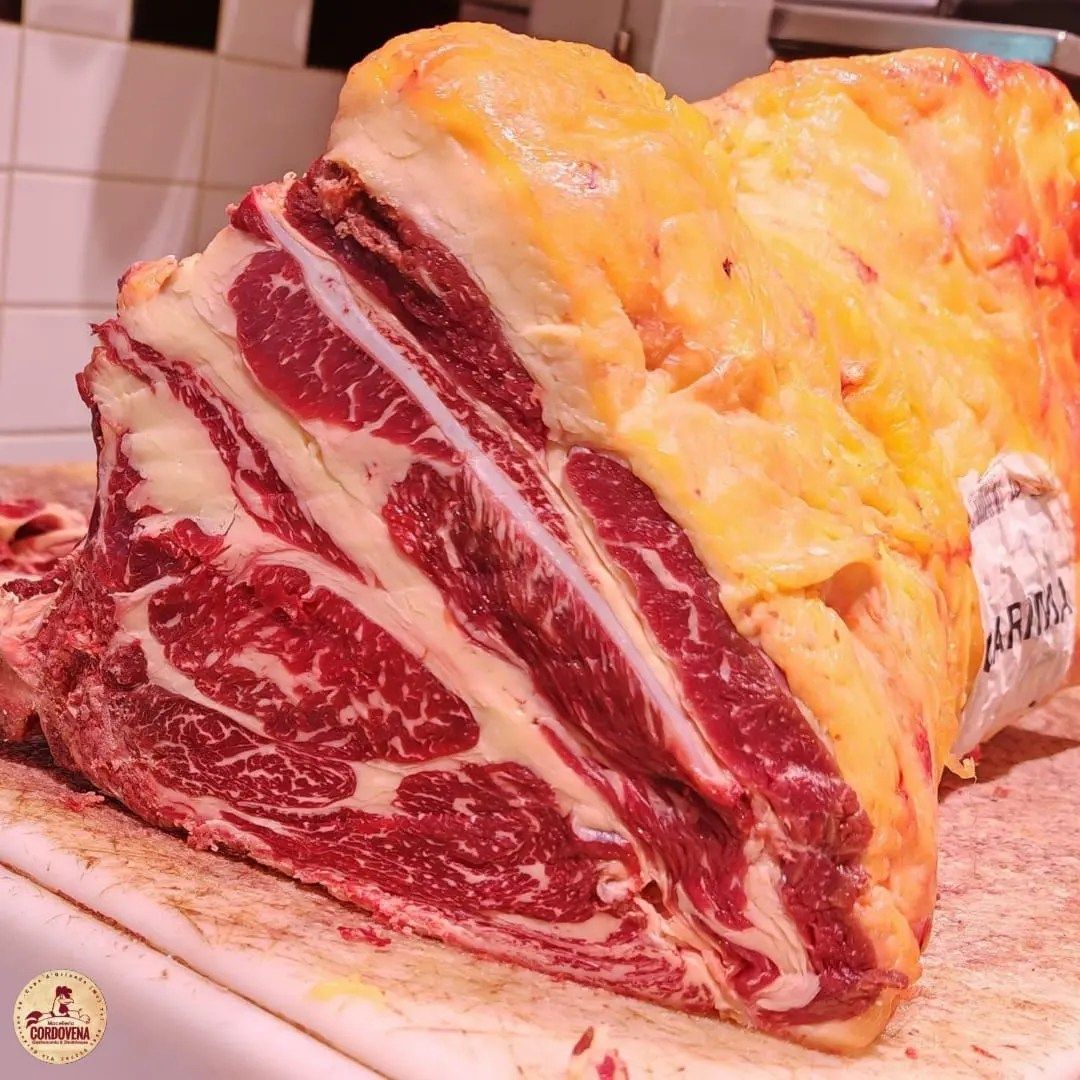 Un grande arrosto di manzo crudo, marezzato di grasso, sul bancone di una macelleria.