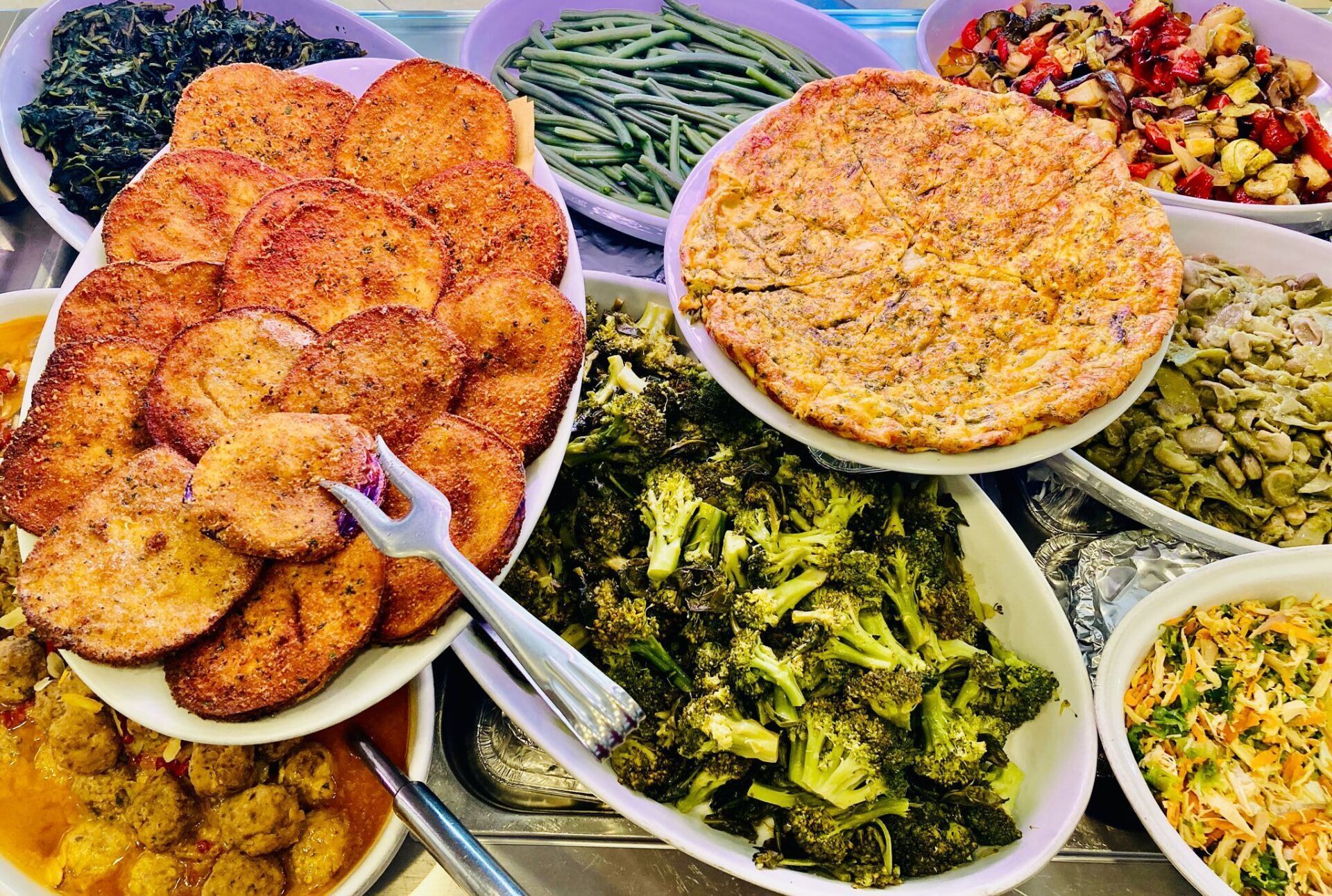 Esposizione a buffet di varie verdure cotte: rondelle fritte, frittata, broccoli, fagioli e altro ancora.