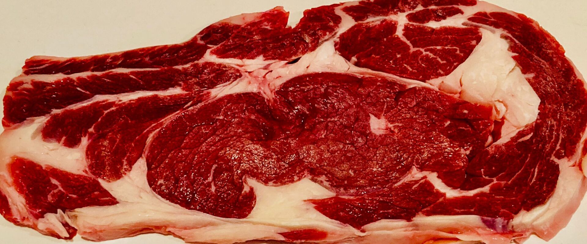 Un taglio crudo di bistecca di ribeye, che presenta carne rossa con marezzature bianche.