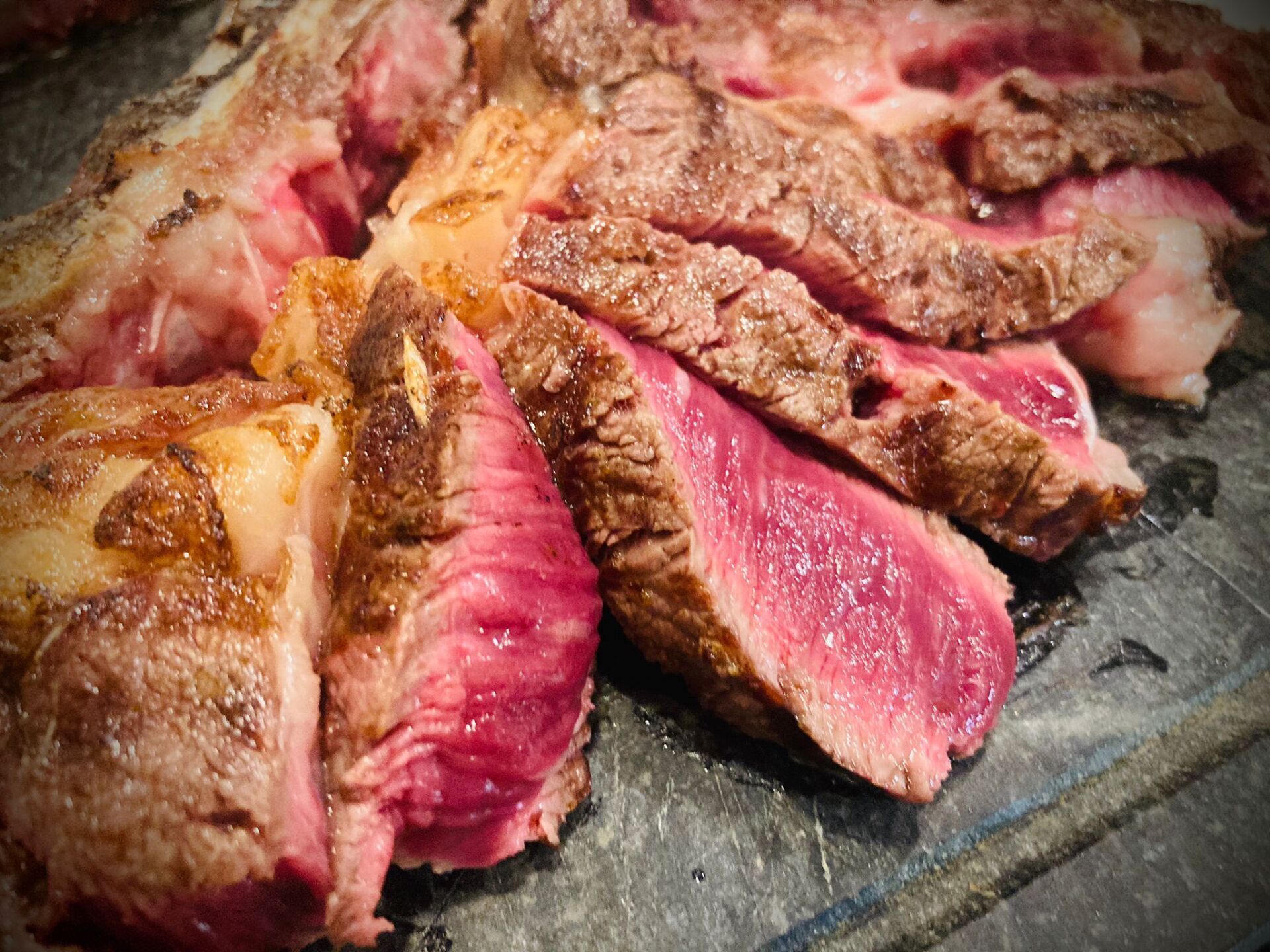 Bistecca tagliata a fette, cotta al sangue, su una superficie grigia, con interno rosa e esterno dorato.