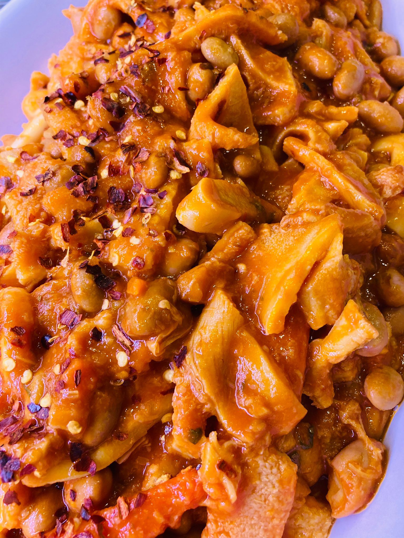 Primo piano di uno stufato caldo e saporito con fagioli e quella che sembra essere trippa, cosparso di fiocchi di peperoncino rosso.