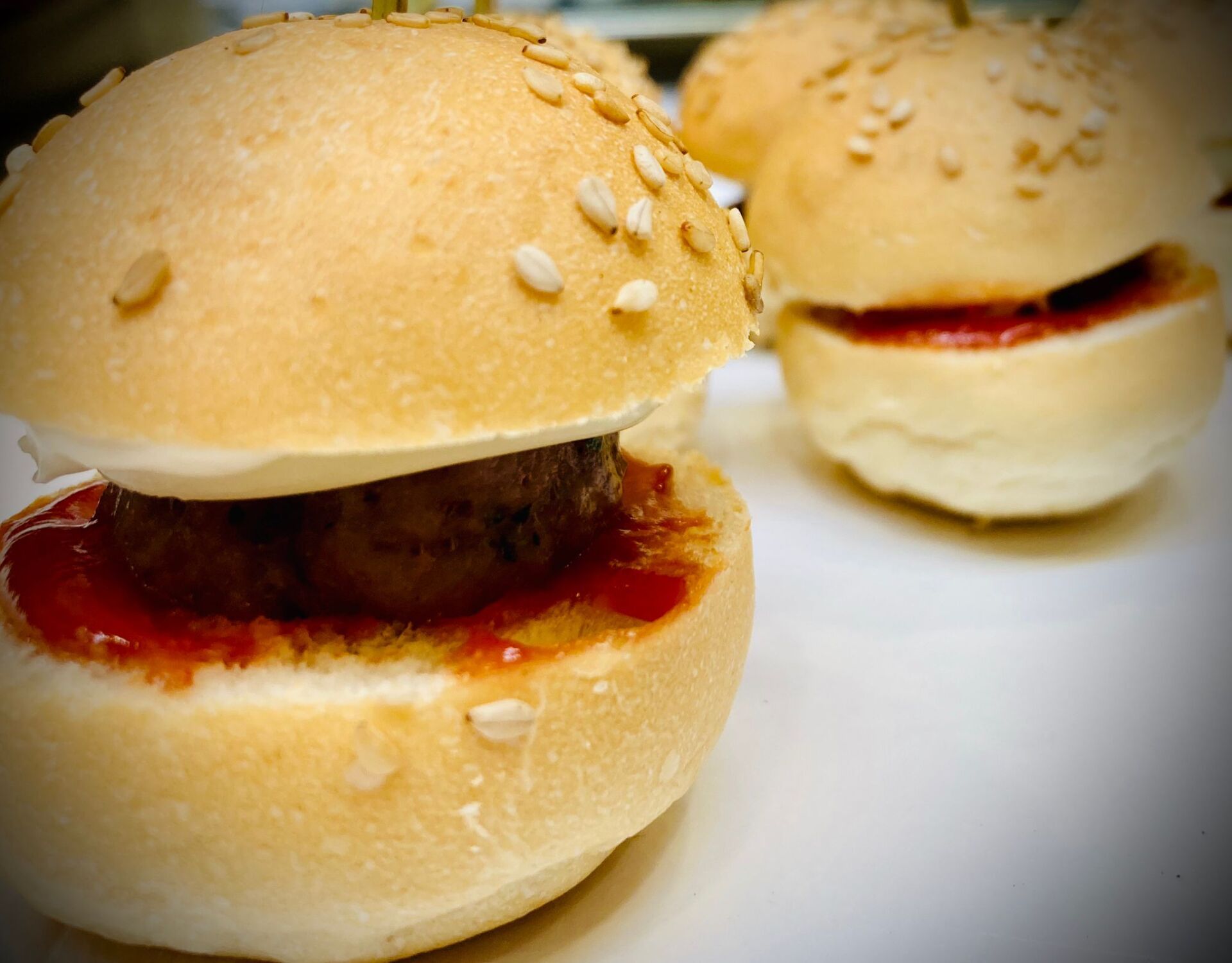 Mini hamburger con panini ai semi di sesamo e salsa rossa.