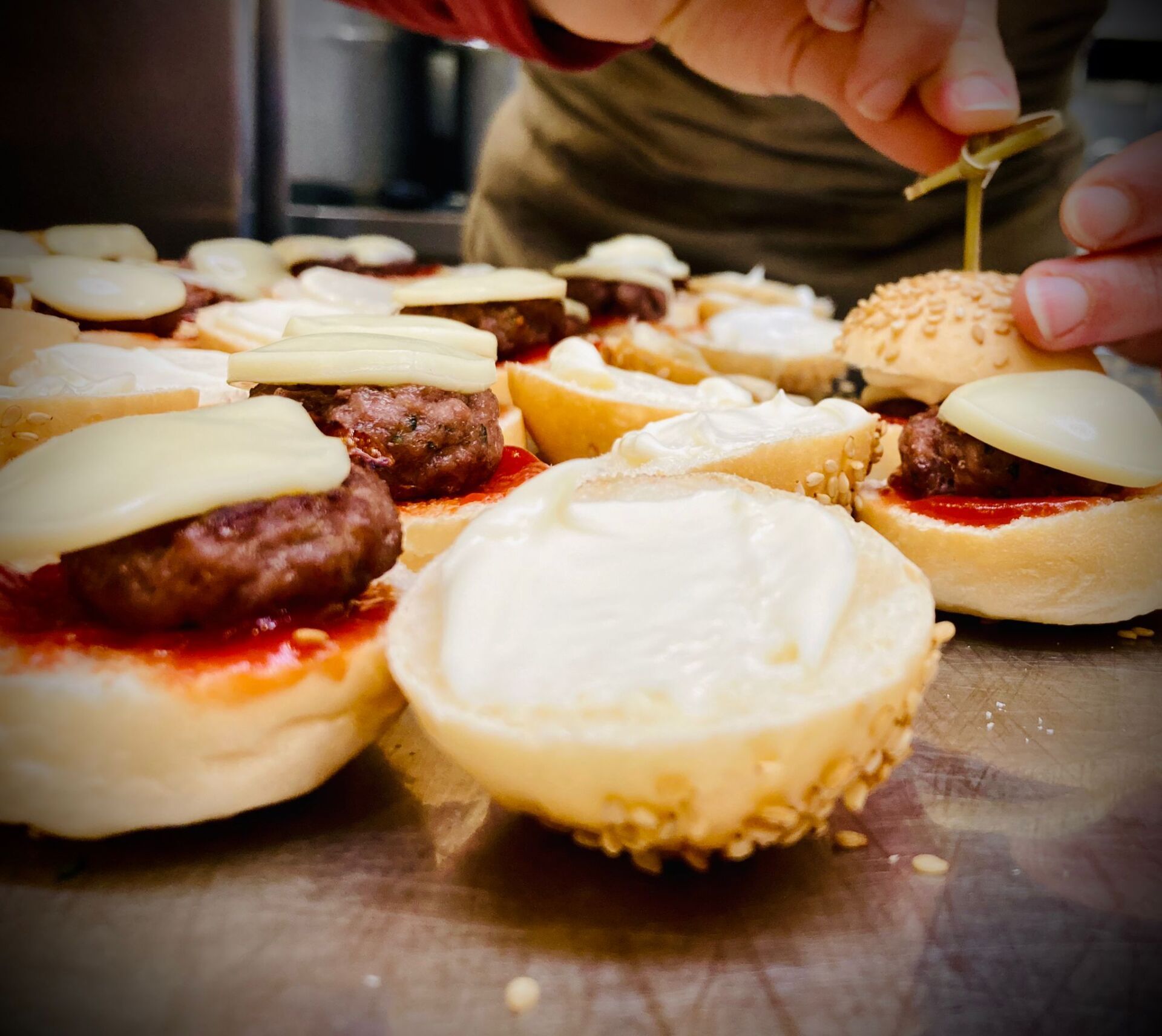 Mini hamburger in fase di assemblaggio, con condimenti e spiedino inclusi.