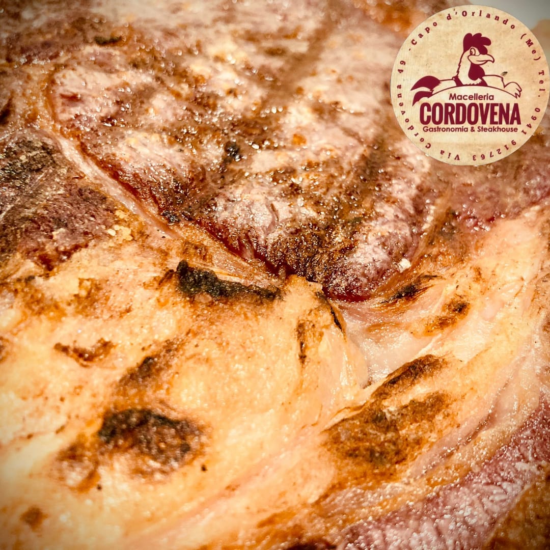 Primo piano di una bistecca alla griglia con osso, che mostra la crosta dorata e il logo Cordovena.
