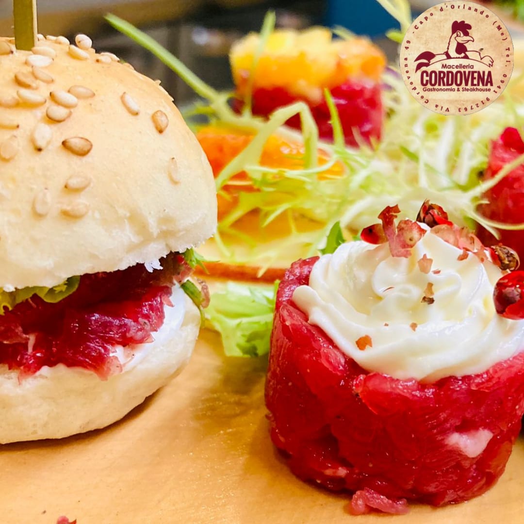 Mini hamburger e piatto di carne con panna, guarnito con verdure, su una superficie di legno.