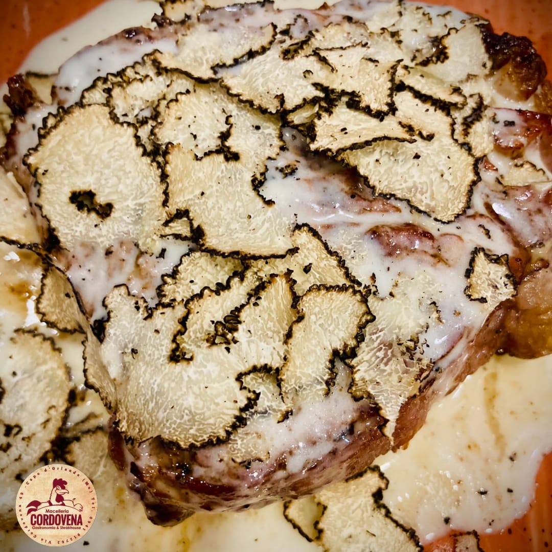 Bistecca guarnita con fettine di tartufo e salsa cremosa su un piatto.