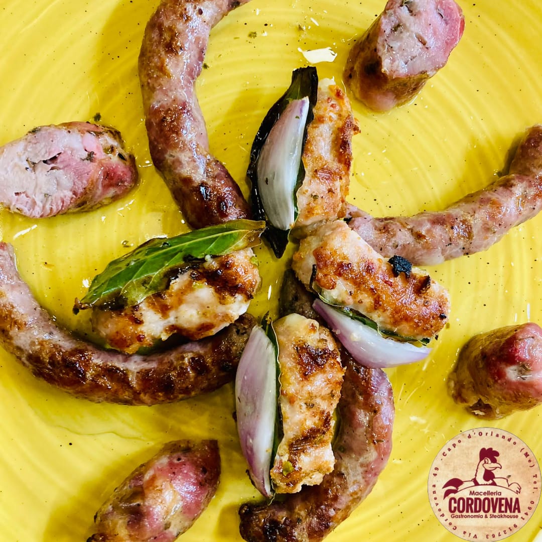 Salsicce grigliate e spicchi di cipolla su un piatto giallo, guarnito con foglie di alloro.