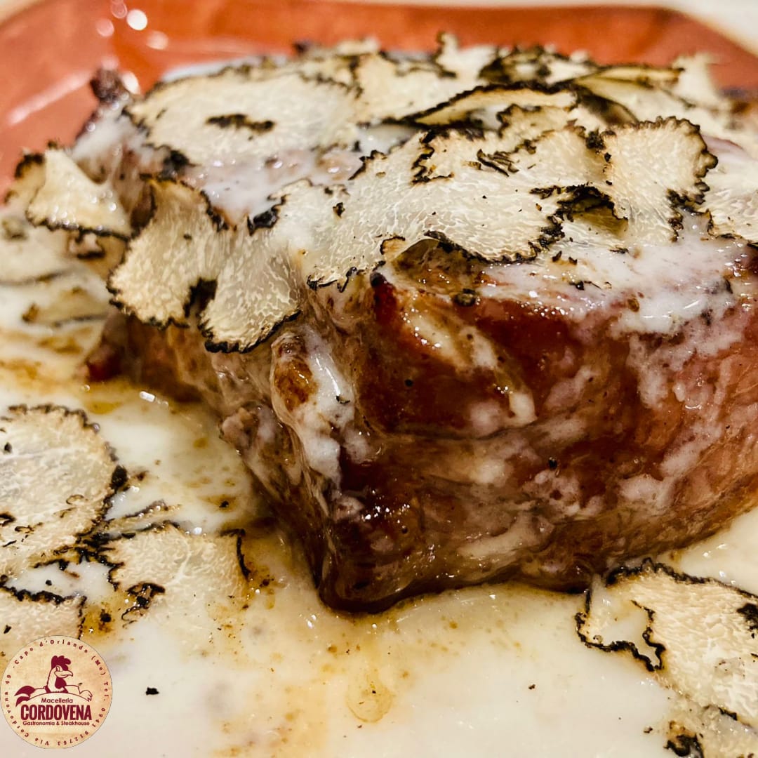 Bistecca guarnita con fettine di tartufo e salsa cremosa su un piatto.