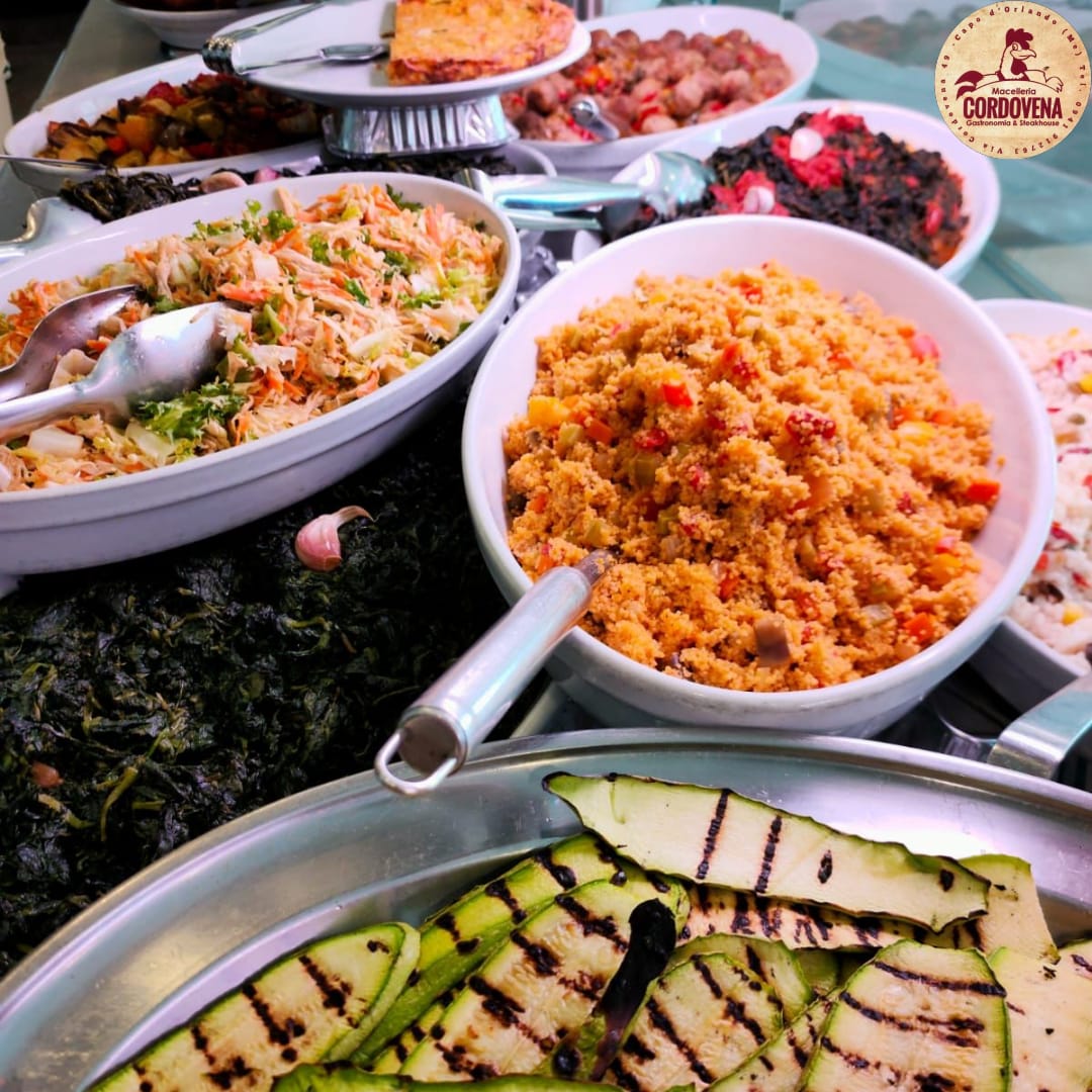 Buffet con vari piatti: couscous, insalate, zucchine grigliate. Il cibo è esposto.