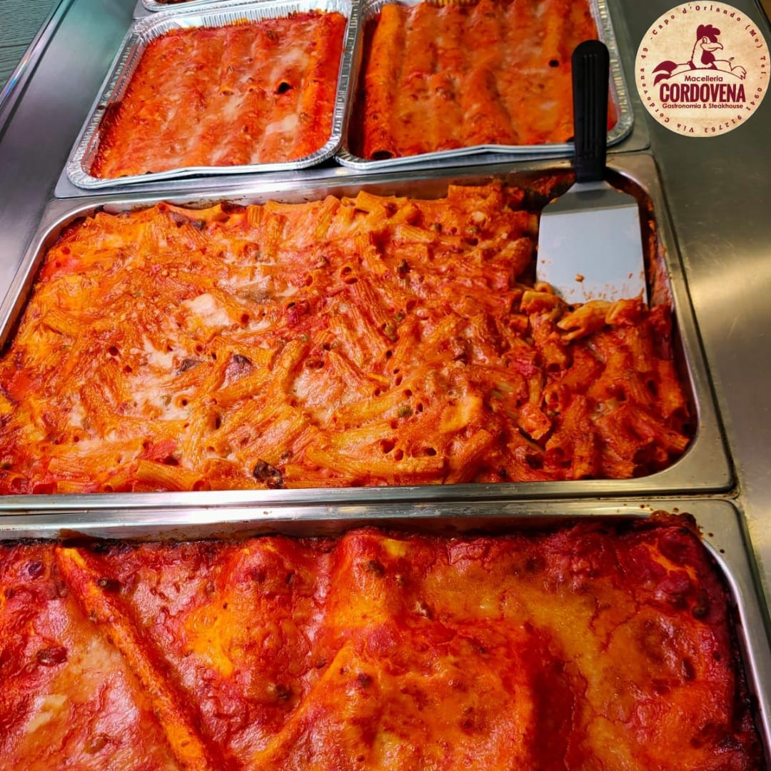Vassoi di piatti di pasta, tra cui lasagne, rigatoni e un altro con salsa all'arancia, in un ambiente da ristorante.