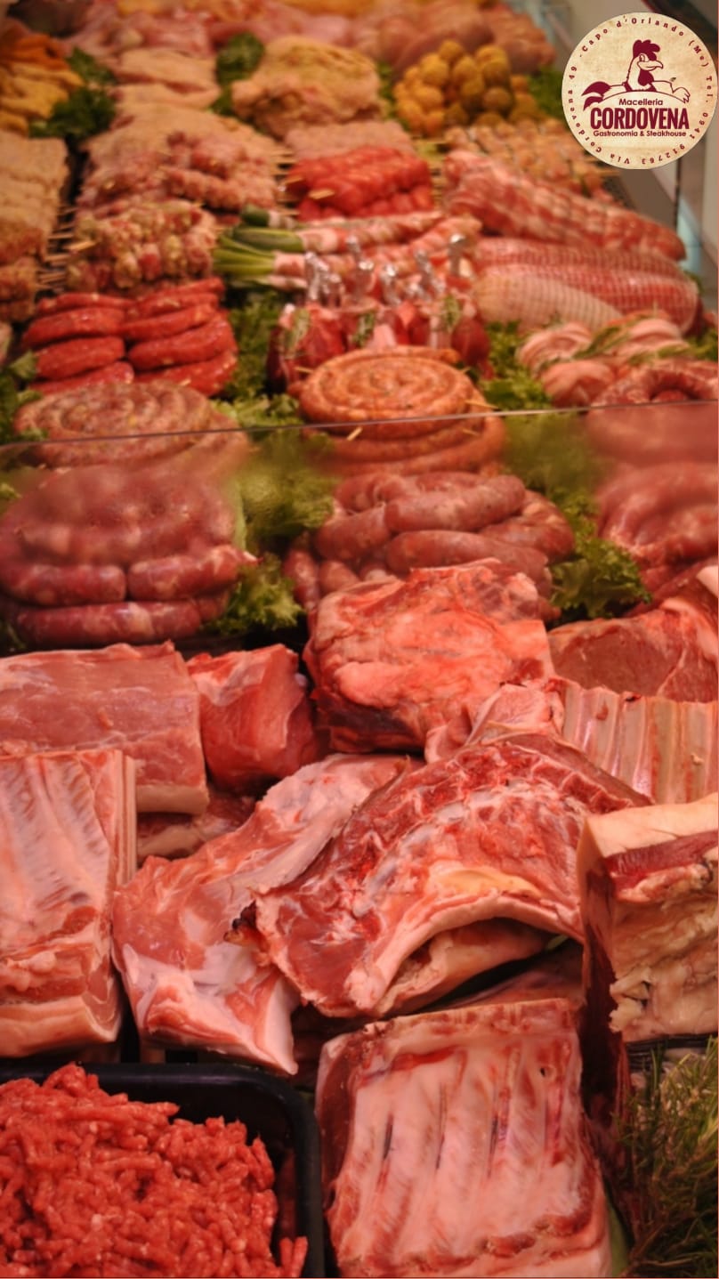 Assortimento di carni crude, tra cui costine, salsicce e carne macinata, esposte in una macelleria.