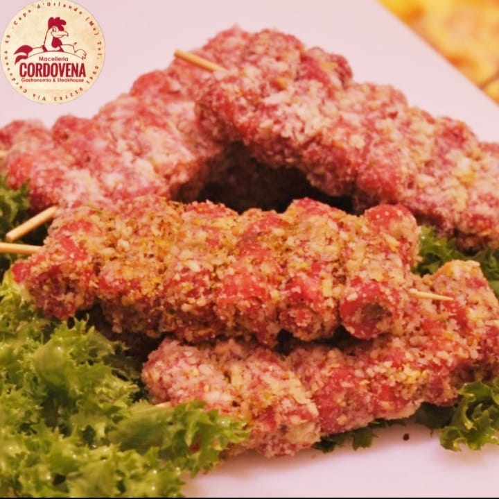 Spiedini di carne impanati, adagiati su un letto di lattuga. Logo Cordovena visibile.