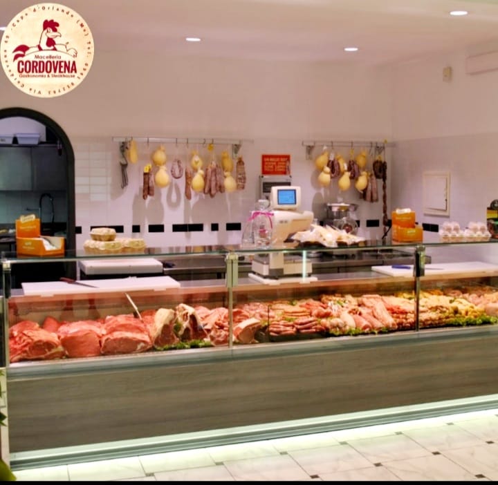 Macelleria con una lunga vetrina piena di vari tagli di carne. Salsicce e formaggi appesi.