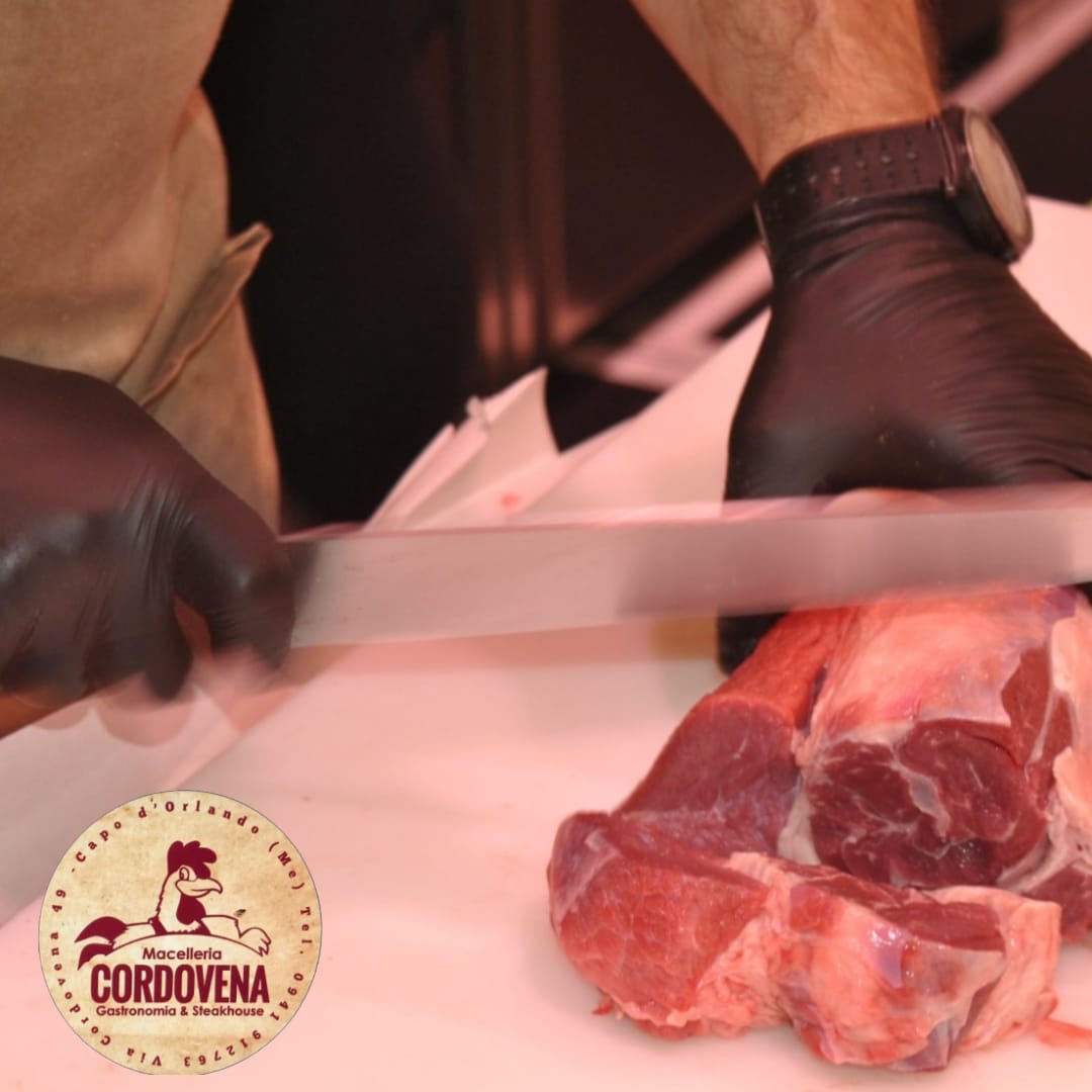 Macellaio che taglia carne cruda su una superficie bianca, indossando guanti neri.