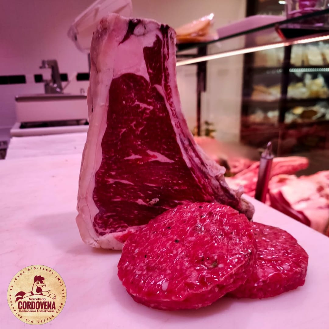 Grande taglio di carne cruda con due polpette su una superficie bianca, con sfondo da gastronomia.