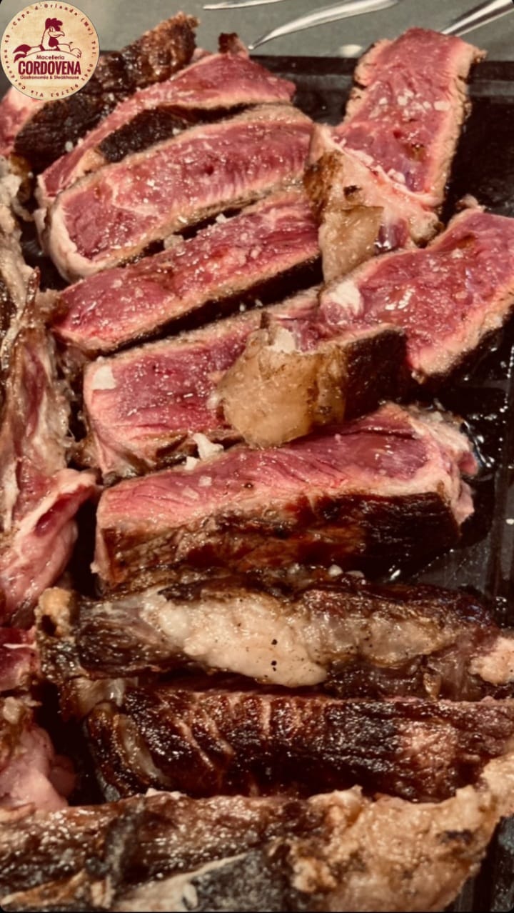 Bistecca tagliata a fette e scottata, con osso visibile e sale grosso, adagiata su una superficie scura.